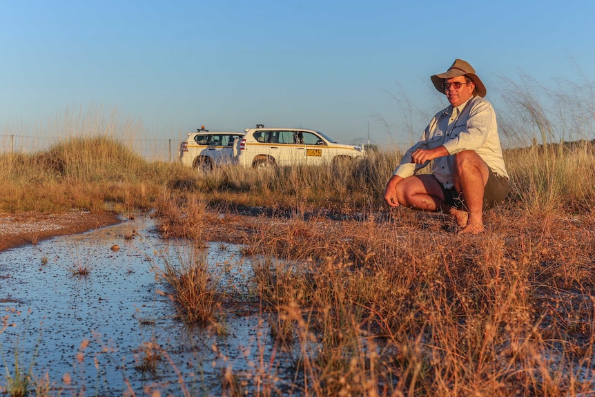 Ecologist Rob Wager kneels next to a small spring against a out-back landscape.