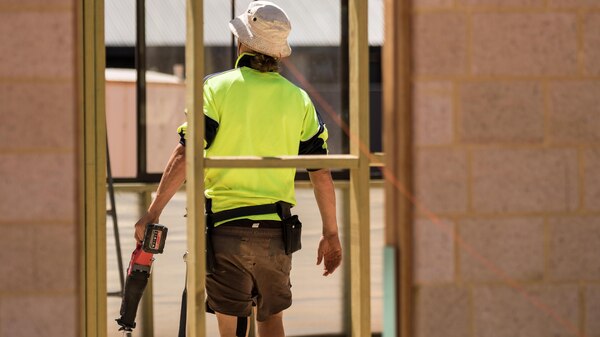 A carpenter carrying a saw on a work site.