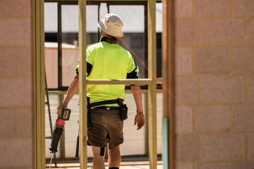 A carpenter carrying a saw on a work site.  