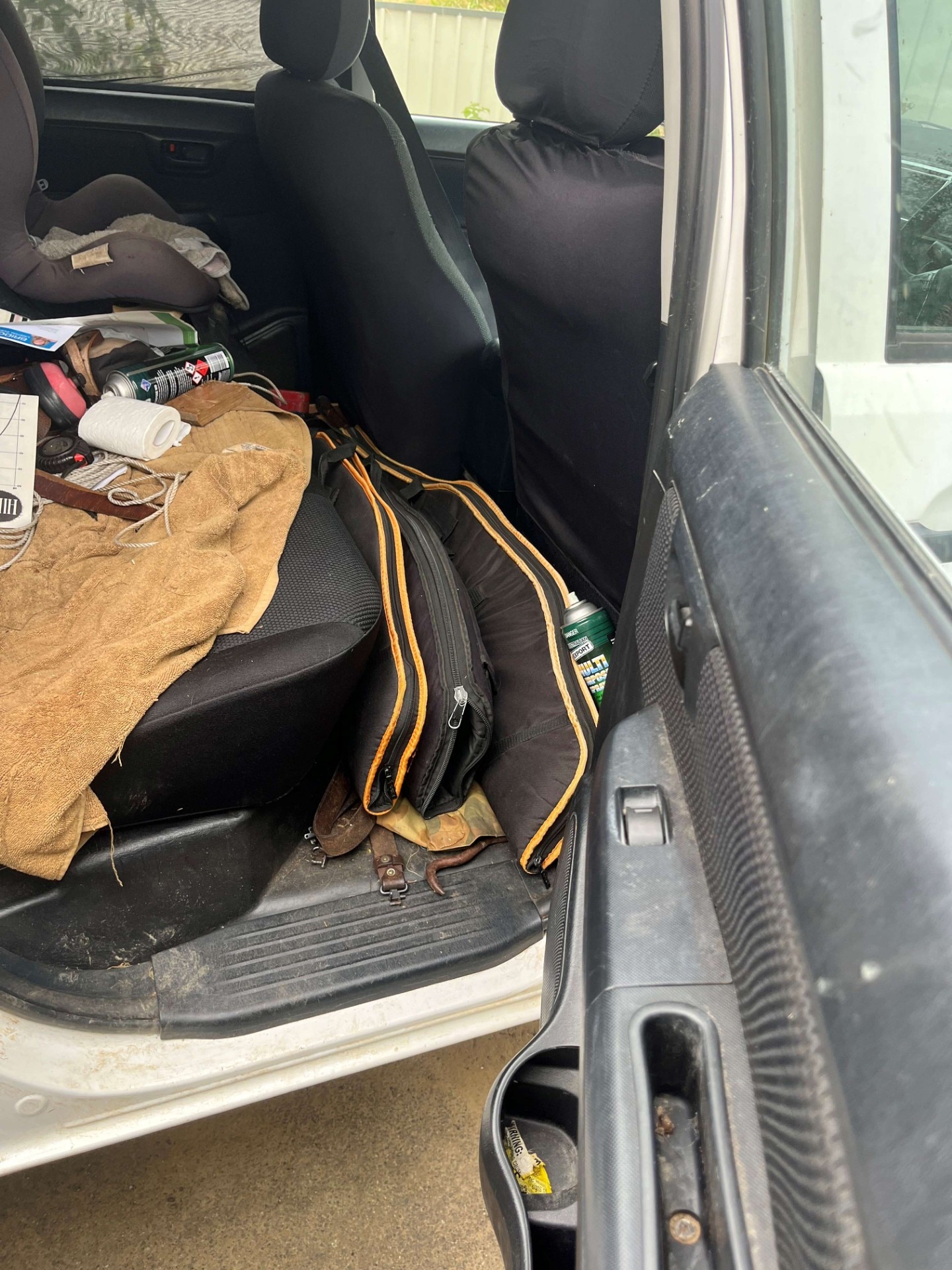 El asiento trasero de un coche con objetos como auriculares, cuerdas y latas de aerosol esparcidos sobre él, así como tres bolsas de armas en el suelo.