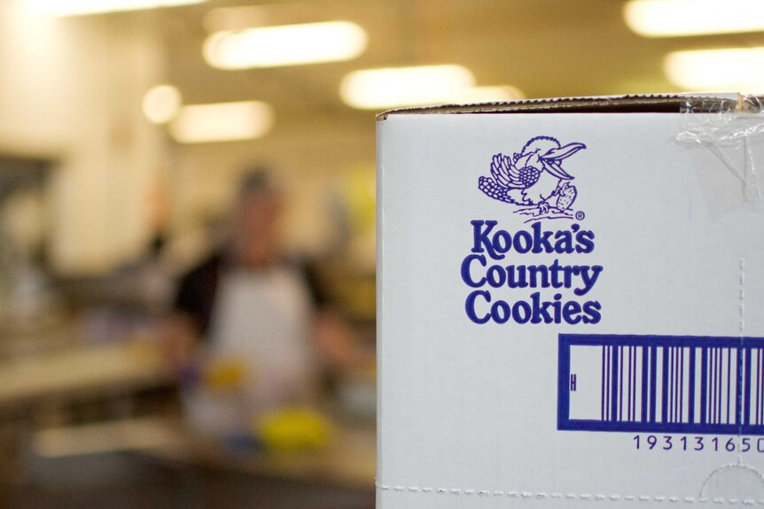 A box of Kooka's Country Cookies sits in front of production line workers.
