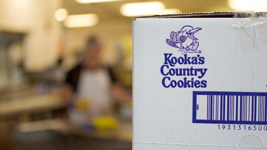 A box of Kooka's Country Cookies sits in front of production line workers.