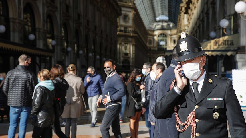 A traffic policeman talks on the phone in front of many people in a busy arcade in Milan.