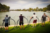 Four penny farthing riders standing on the banks of the Murray River.