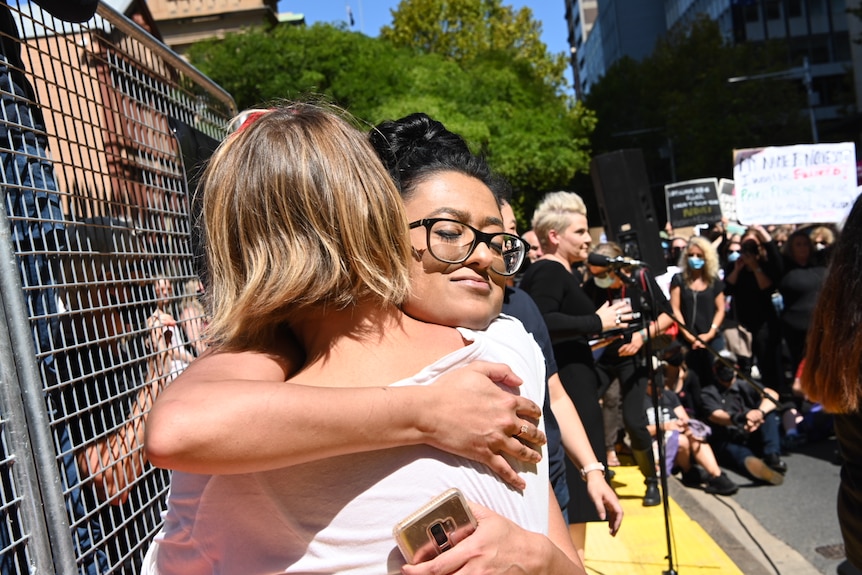 Two protest attendees embrace, one wears glasses