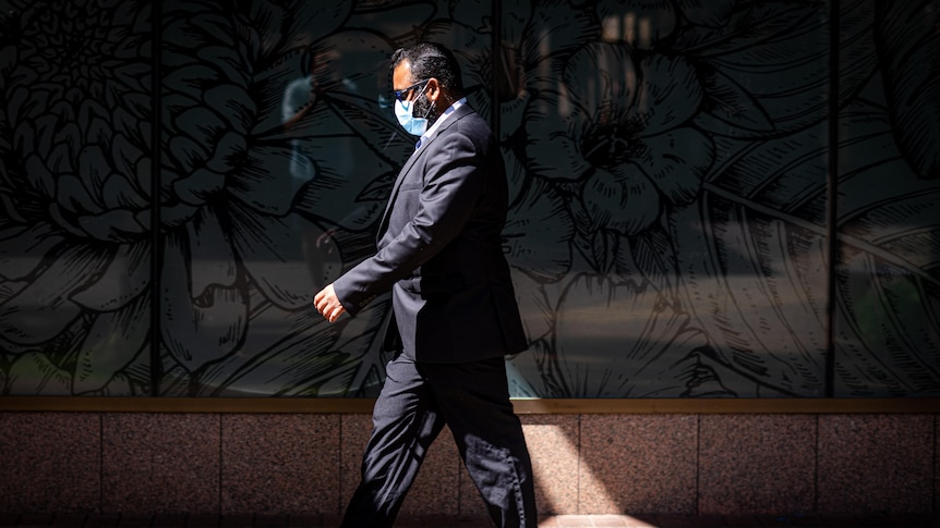 A man is wearing a mask and walking down a street.