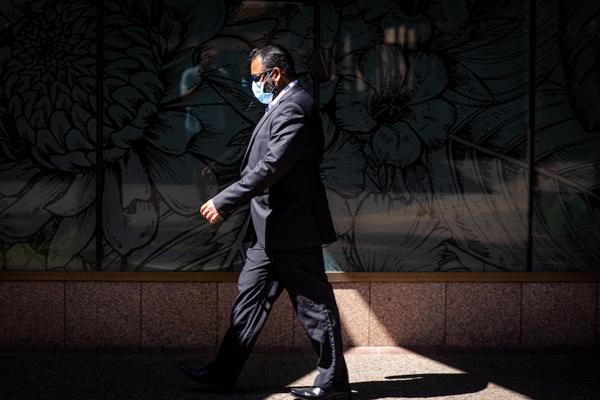 A man is wearing a mask and walking down a street.