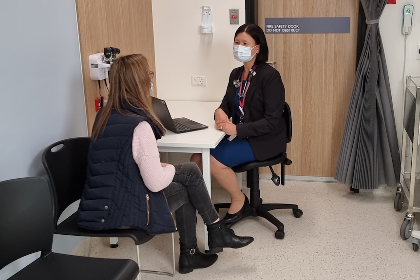 A female doctor speaks to a female patient in a room.