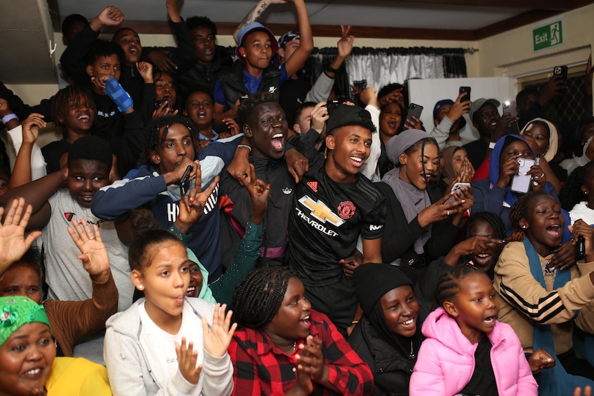 A group of people in a group excited and cheering watching a television out of frame