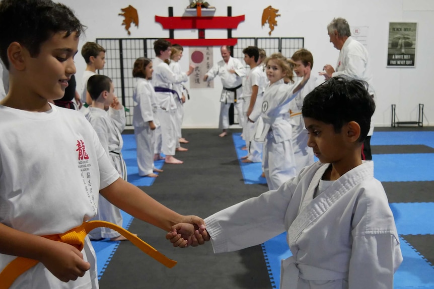 Two boys stand face to face, one holding the other's wrist, in a martial arts class.