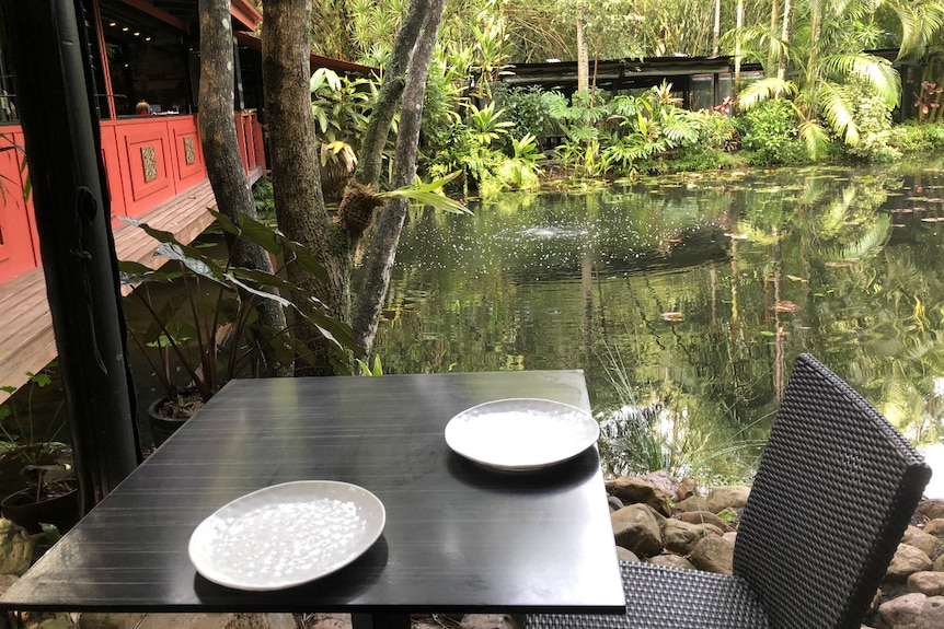 A restaurant table overlooking a tranquil pond surrounded by lush tropical plants.