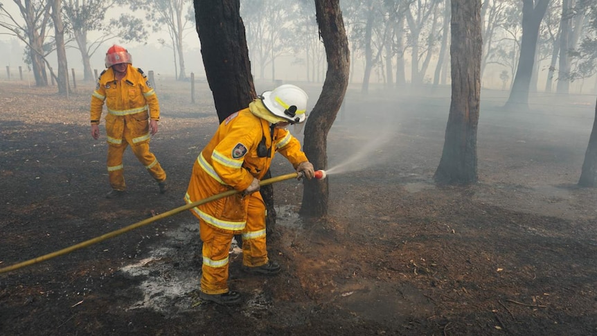 A man with a hose sprays a fire with water.