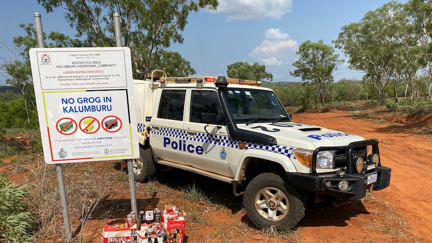 Bottles of alcohol stacked near a police four wheel drive and a sign, which stipulates no alcohol is allowed in the community.