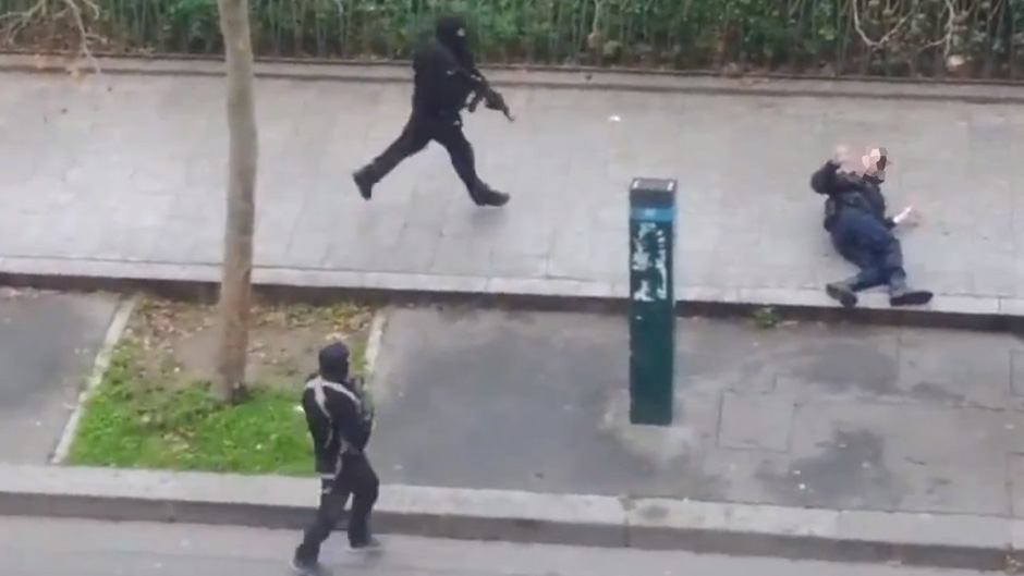 An injured police officer on the ground outside the Charlie Hebdo office, as masked gunmen approach. (Facebook/Jordi Mir)