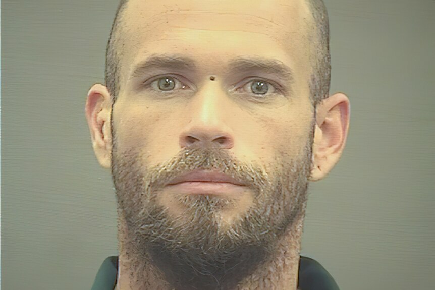 Jacob Chansley appears in a mug shot with beard and shaved head.
