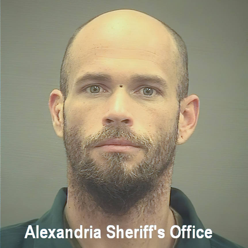 Jacob Chansley appears in a mug shot with beard and shaved head.