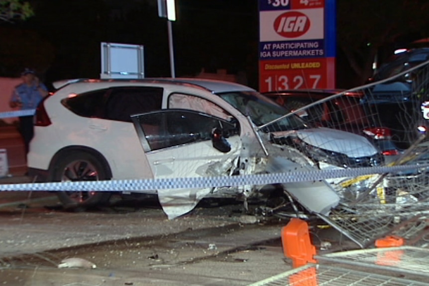 A white hatchback crashed into a fence, with police tape in the foreground.