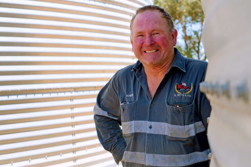 Robert Kitto stands beside water tanks smiling about his recent harvest.