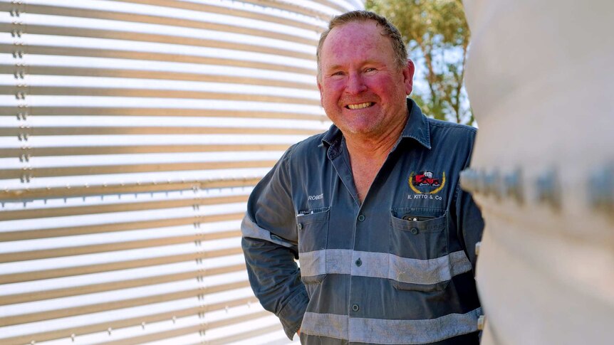 Robert Kitto stands beside water tanks smiling about his recent harvest.