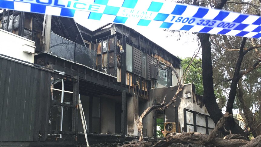 A two-storey house with clear fire damage, surrounded by police tape.