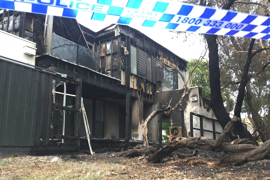 A two-storey house with clear fire damage, surrounded by police tape.