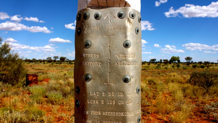 A metal plate from 1960 nailed to a white post with details of the border location engraved.