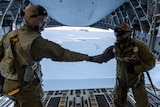 Crew members shake hands inside a military aircraft with rear door open.