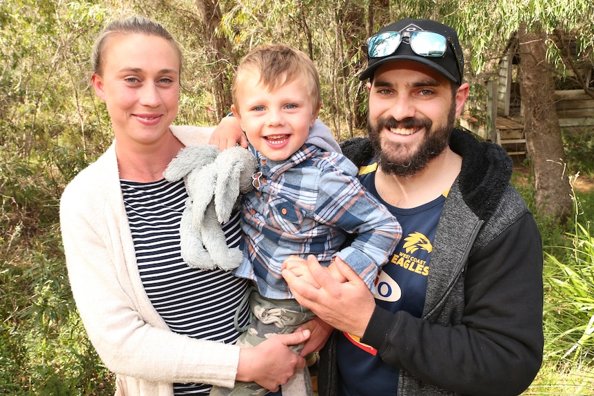 A woman and a man stand either side of a small boy in a family portrait.