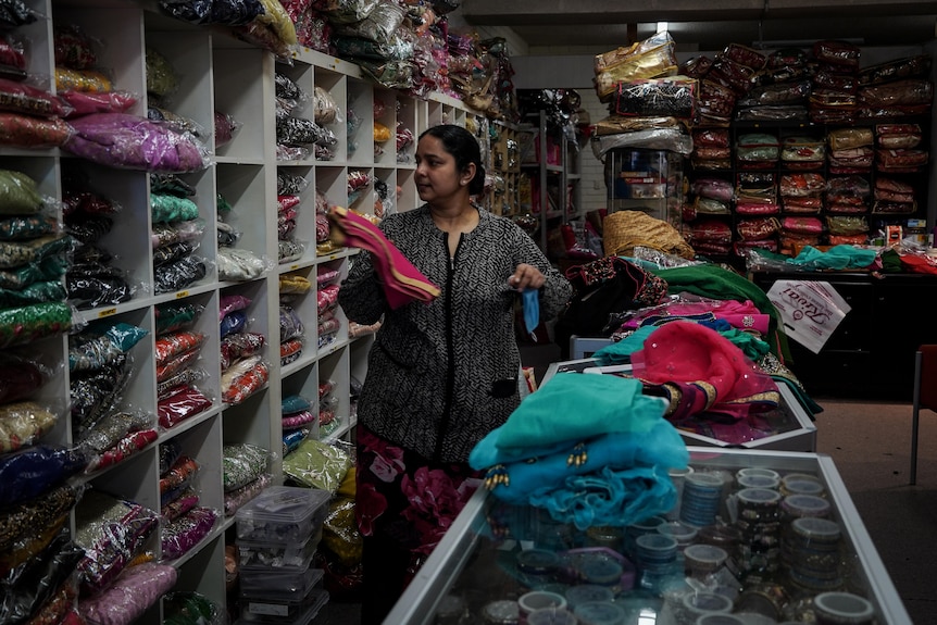 Manpreet puts a folded dress onto shelf her shop.