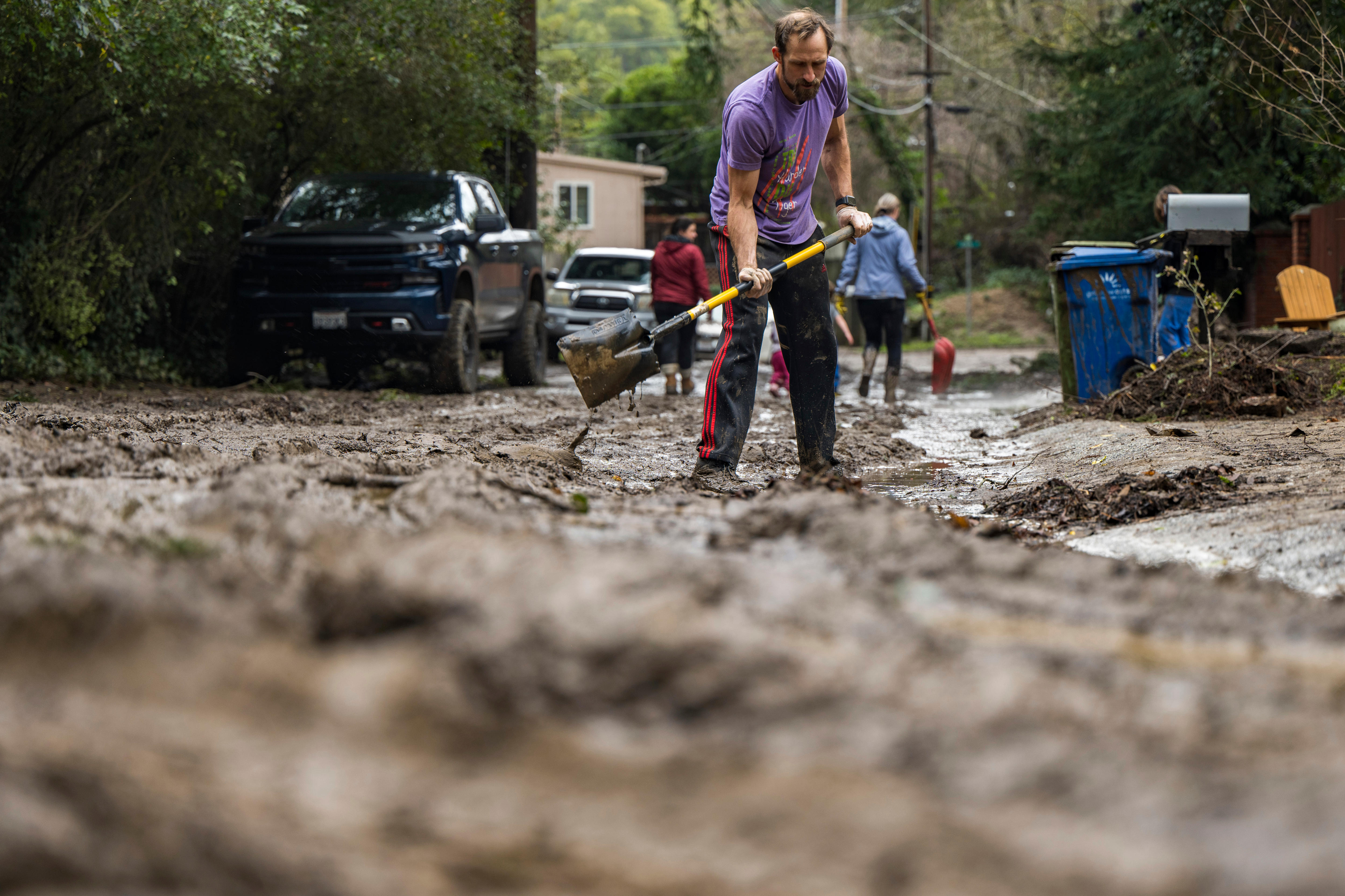 A man in a purple shirt shoveling mud