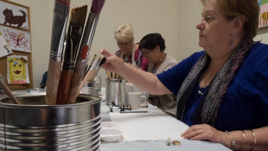 Janice Phillips reaches for a paint brush at the Muscular Dystrophy SA art therapy class