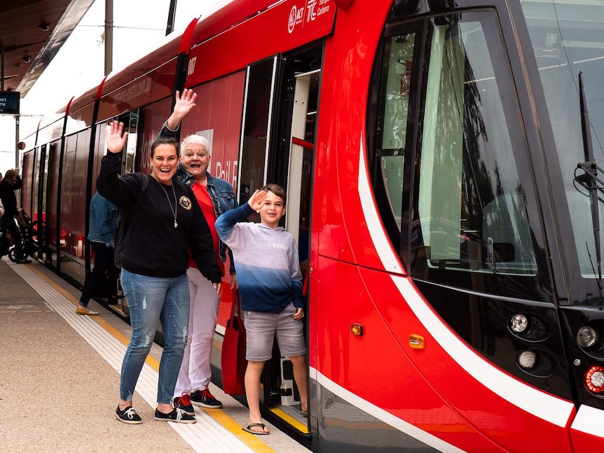 People waving as they get onto a red light rail vehicle in Canberra.