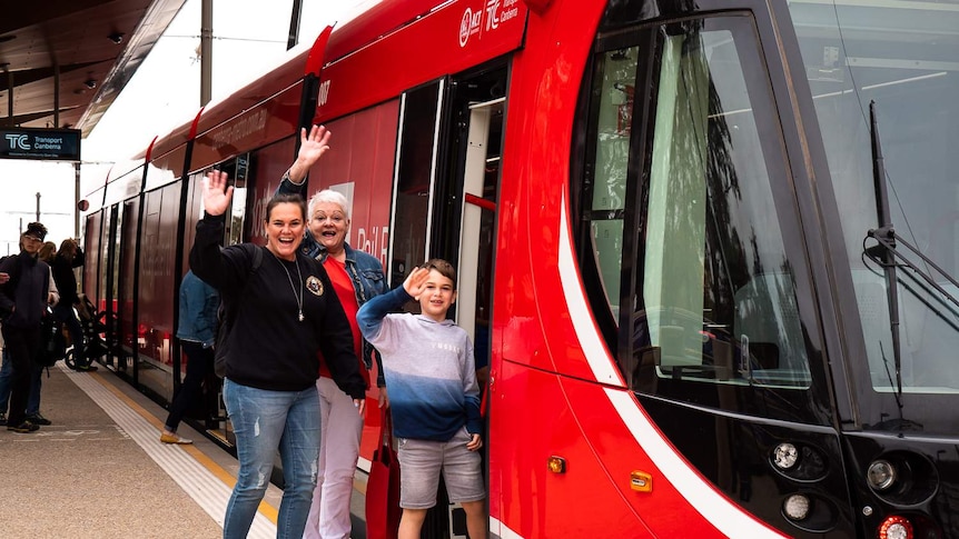 People waving as they get onto a red light rail vehicle in Canberra.