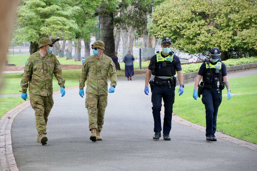 Two ADF officers wearing fatigues and masks walk alongside two Victoria Police officers.