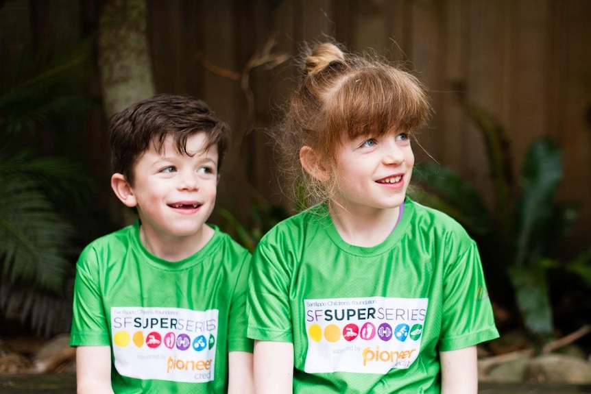 A young brother and sister sit alongside each other in green matching shirts.