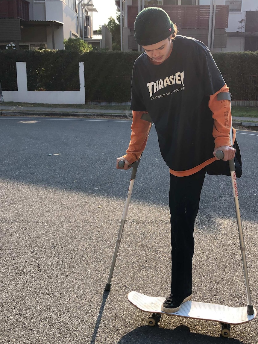 Leg amputee Ned Desbrow stands on a skateboard with crutches.