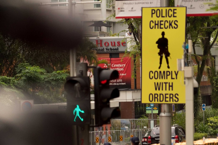 huge concrete barriers divide a busy road, as people walk below a sign that says police checks, comply with orders