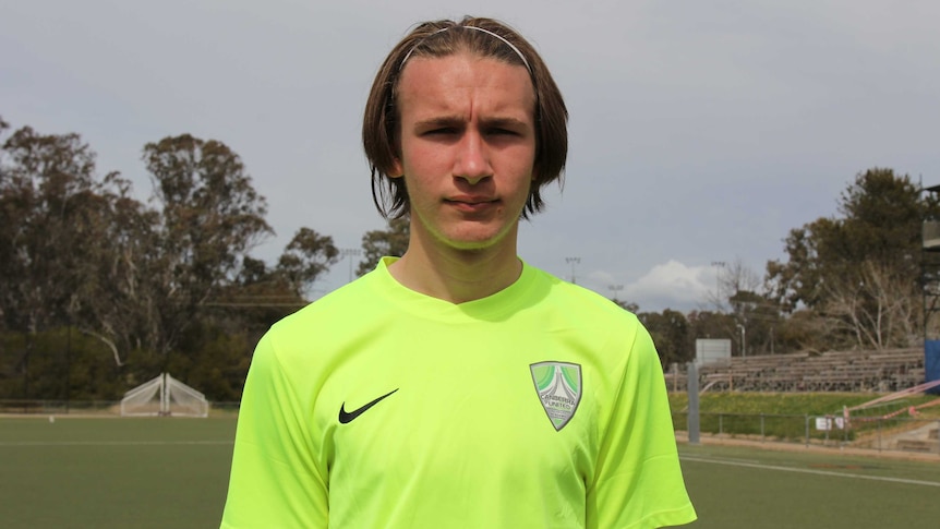 A boy in a soccer jersey stares into the camera