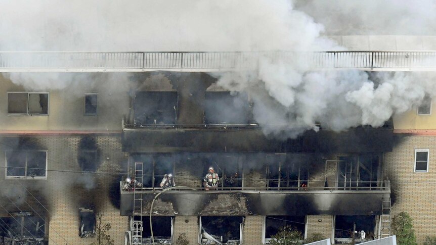 Firefighters stand in a charred building, grey smoke rises.