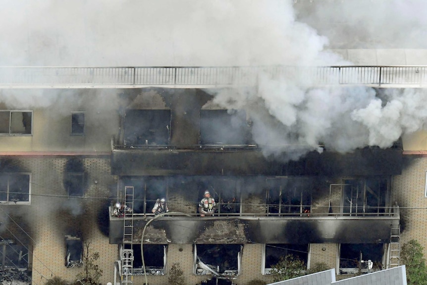 Firefighters stand in a charred building, grey smoke rises.