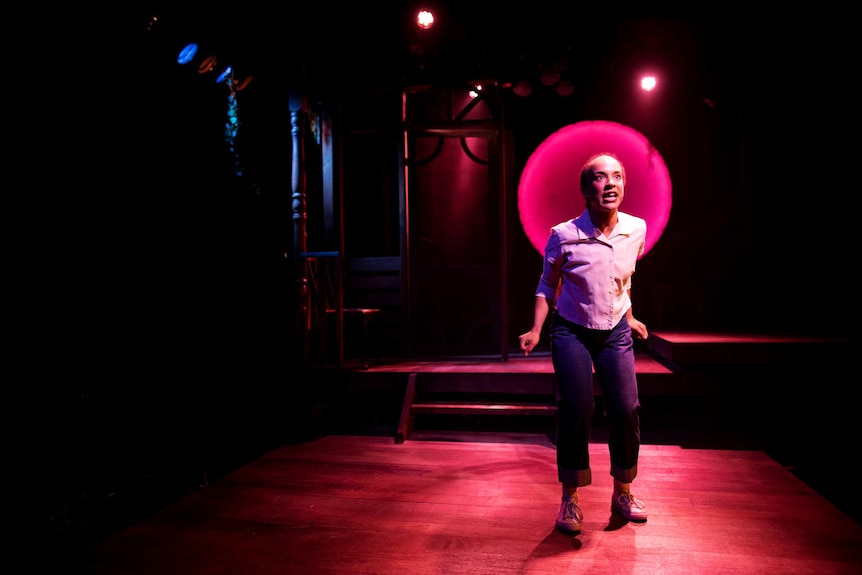 A woman singing on stage, lit by pink lights