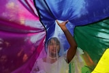 A person stand under a rainbow flag in a wedding dress