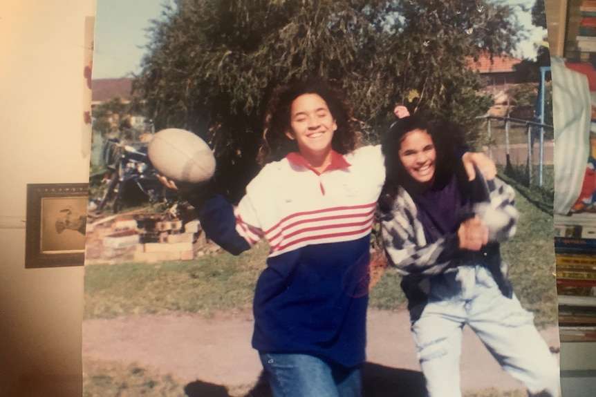 Young Megan in a jersey holding a football, arm around another young girl.