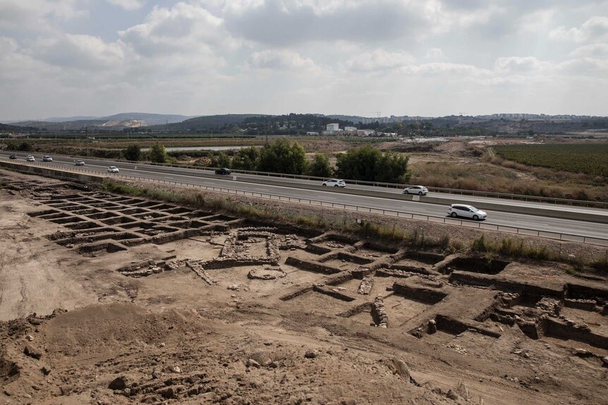 A patch of dirt next to a highway is excavated and shows evidence of what looks to be an ancient city.