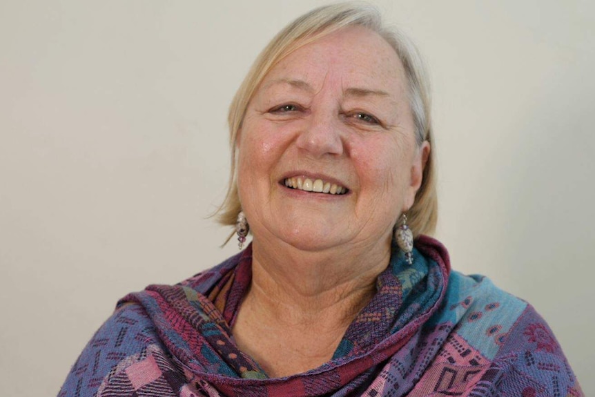 A head and shoulders image of a smiling middle-aged woman wearing earrings and a shawl.