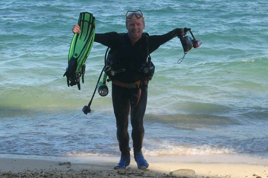 a man wearing scuba gear holds up equipment while standing in the ocean