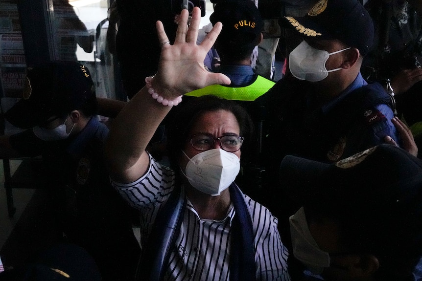 Leila De Lima wearing a mask waves amid a crowd of people.  