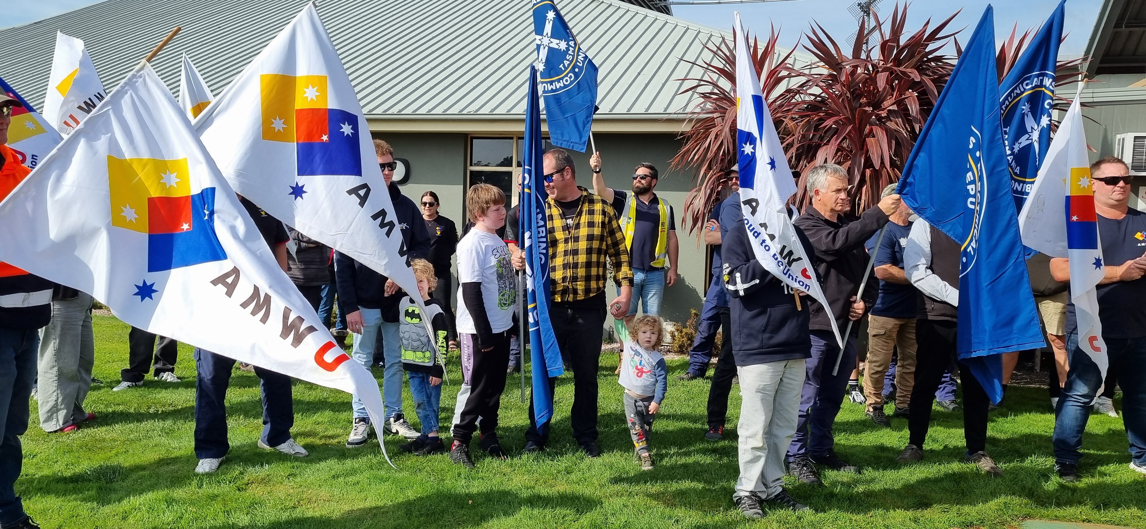Crowd of workers holding union flags and slogans gather on green lawn
