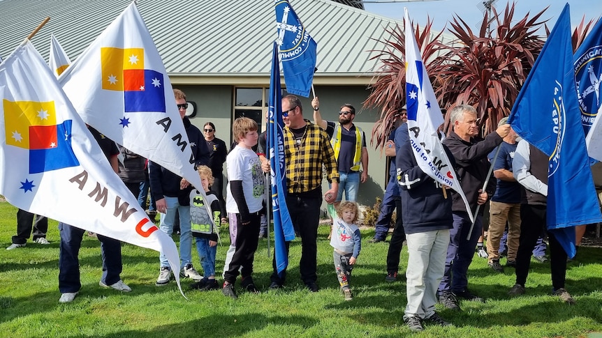 Crowd of workers holding union flags and slogans gather on green lawn