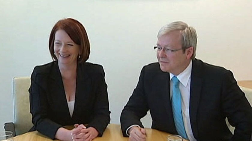 Julia Gillard smiles while Kevin Rudd looks forlorn, the two of them sitting side by side at a table looking at maps.